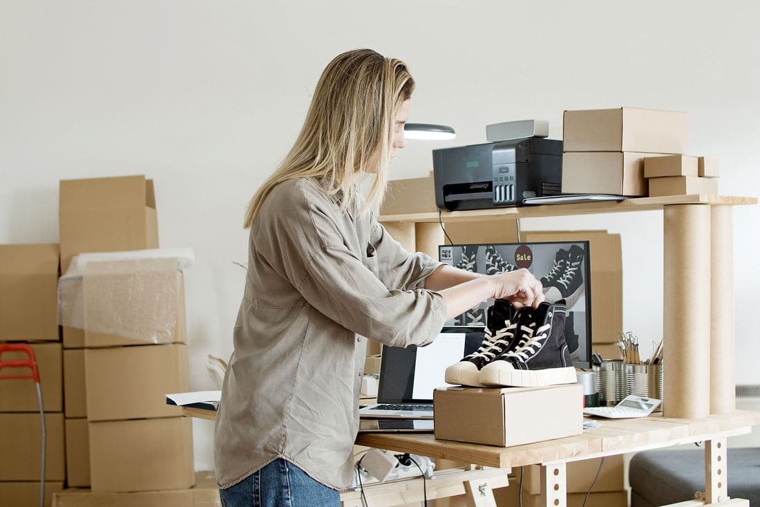 A reseller photographing trainers in a home workspace stacked with parcels